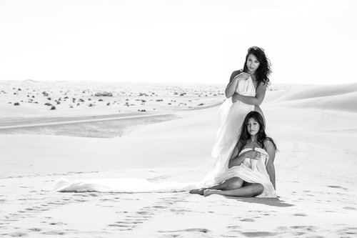 Monochrome photograph of two women wrapped in white fabric posed on sand dunes in a vast desert landscape