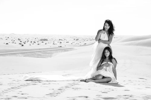 Monochrome photograph of two women wrapped in white fabric posed on sand dunes in a vast desert landscape
