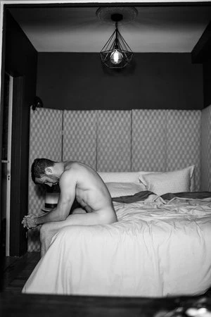 Monochrome portrait of a man seated on a made bed in a bedroom, photographed by Alvin Nguyen in Los Angeles.