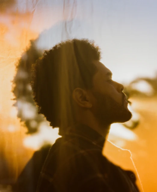 Close-up portrait of an adult Black man looking upward in golden hour lighting with sunlight and shadows on his face and neck.
