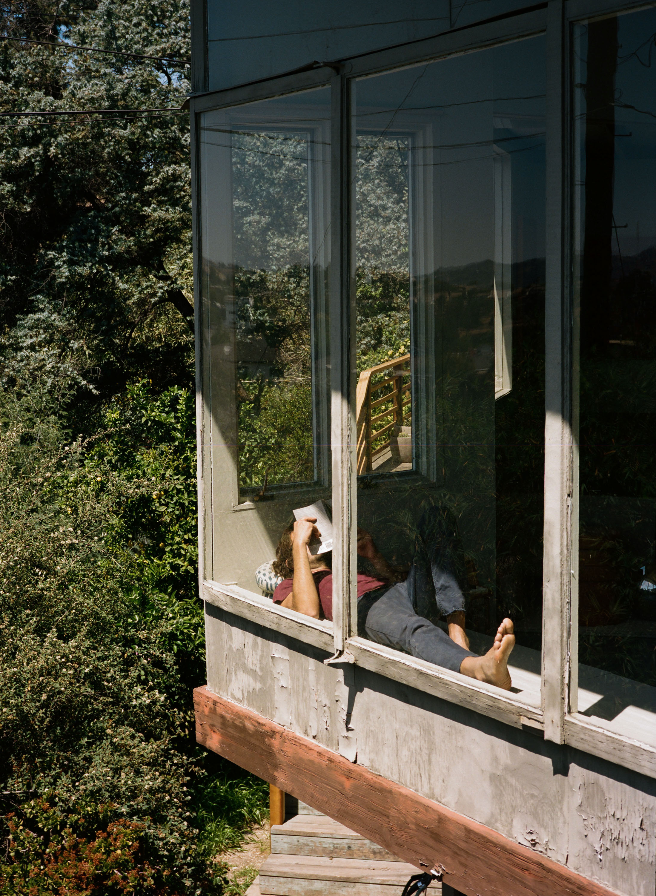 Adult relaxing indoors near a window with a book, enjoying natural light and a view of trees outside, creating a peaceful scene.