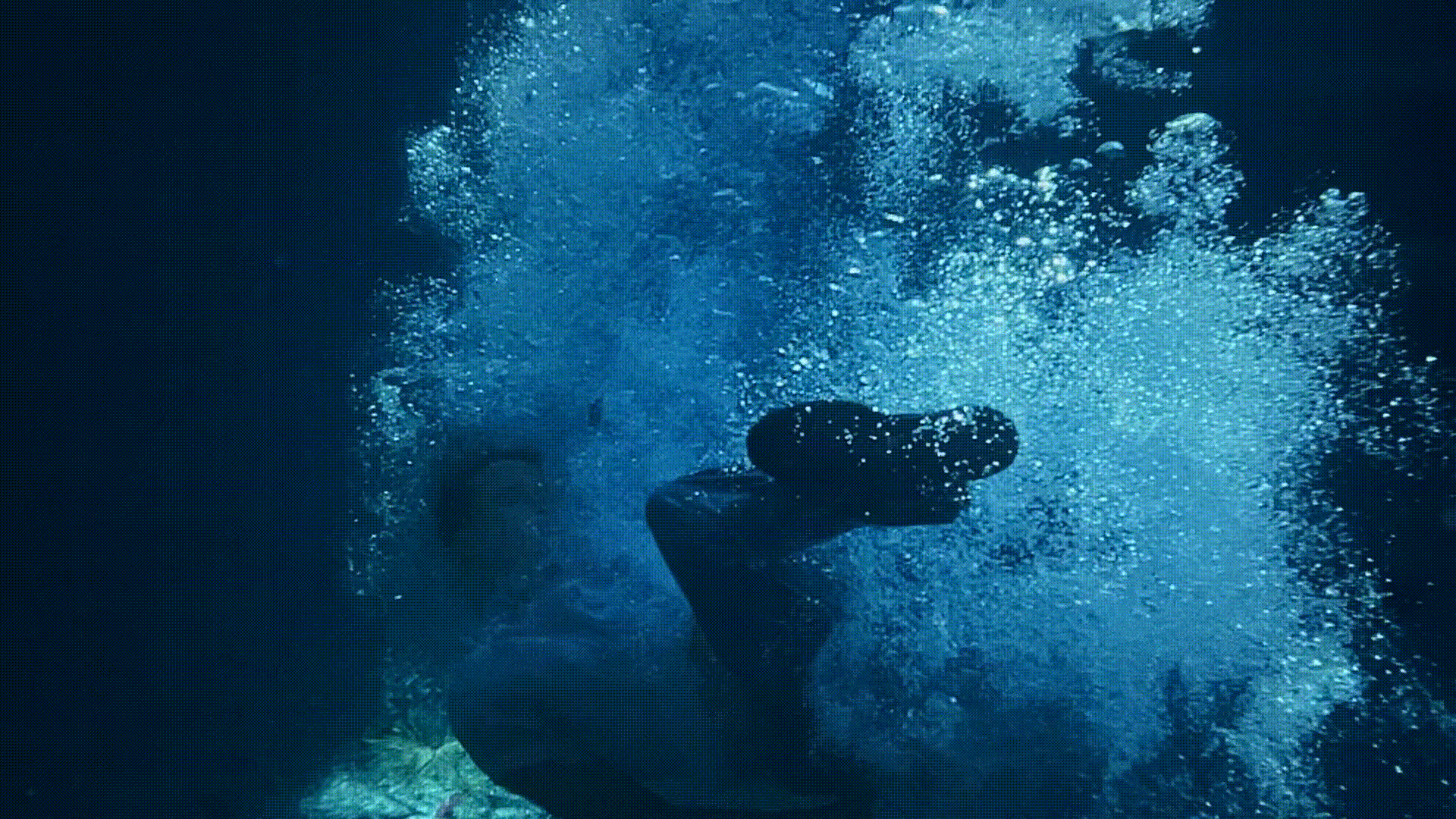 Person swimming underwater in blue ocean. Bubbles surround them. Underwater photography of person diving into water.