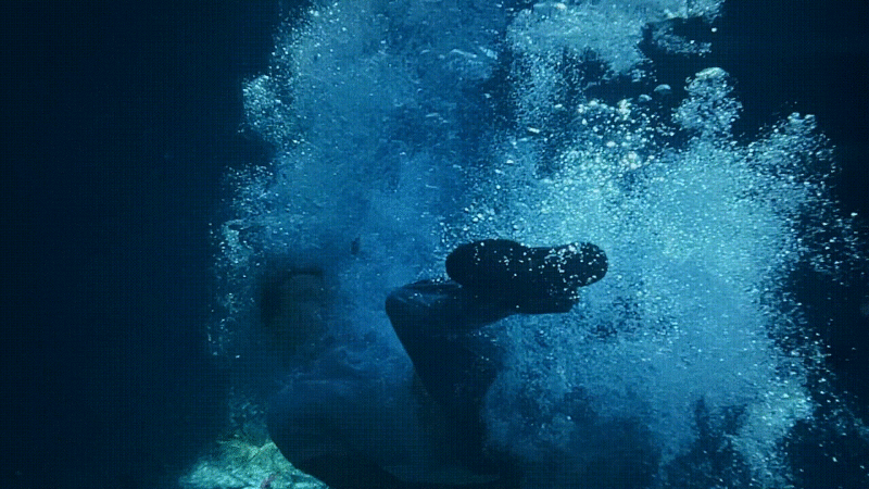 Person swimming underwater in blue ocean. Bubbles surround them. Underwater photography of person diving into water.
