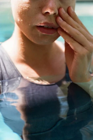 Close-up portrait of a woman standing in water wearing a dark swimsuit with water droplets on her skin.