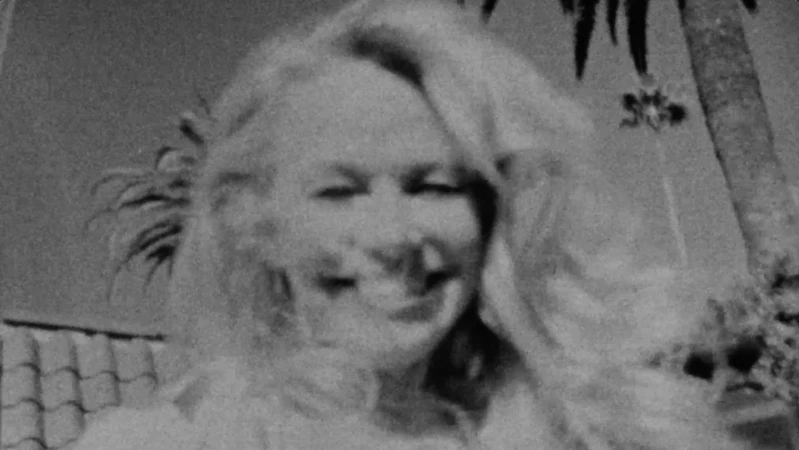 Monochrome portrait of a smiling blonde woman outdoors with palm trees visible in the background grain