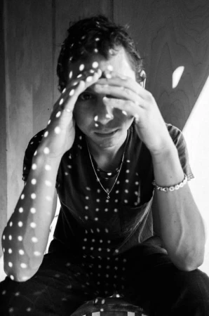 Portrait of a man holding his head with hands, dappled with dot-patterned light by photographer Chantal Anderson.