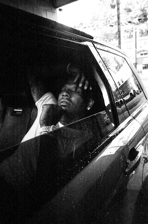 Adult male in car interior with hand on head. The monochrome photo is in low light with dark windows reflecting outdoor light.