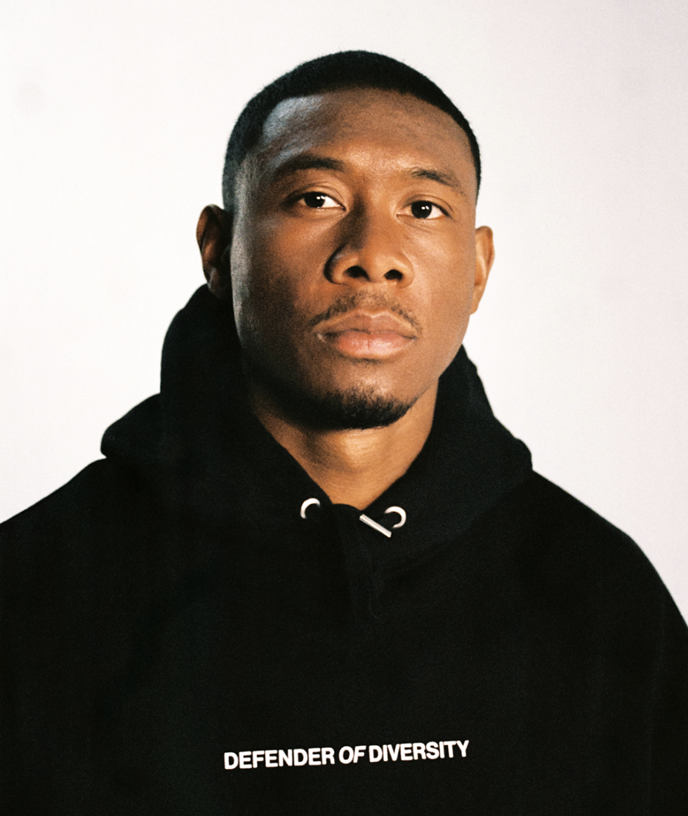 Headshot of a young adult black man wearing a black hooded sweatshirt with white text on a white background in portrait orientation.