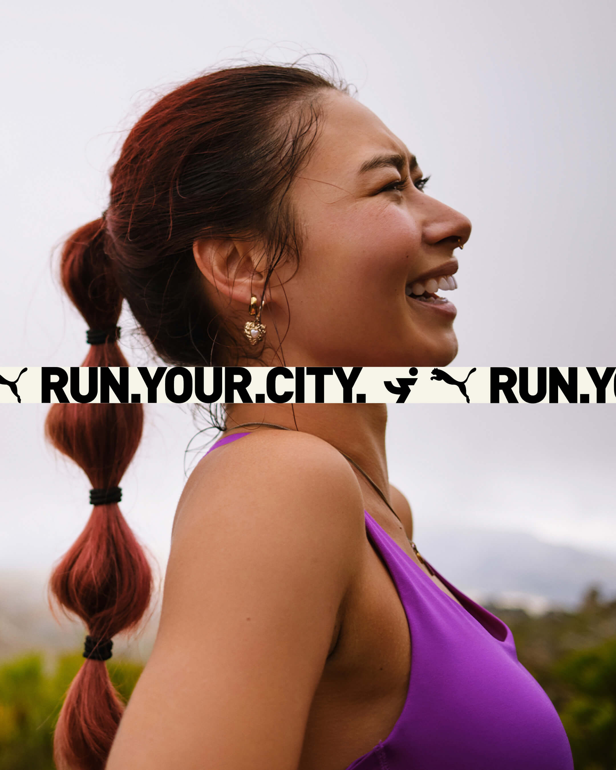 Portrait of a smiling Asian woman with a ponytail, wearing a purple sports top, and running outdoors in a nature setting with blurred background.