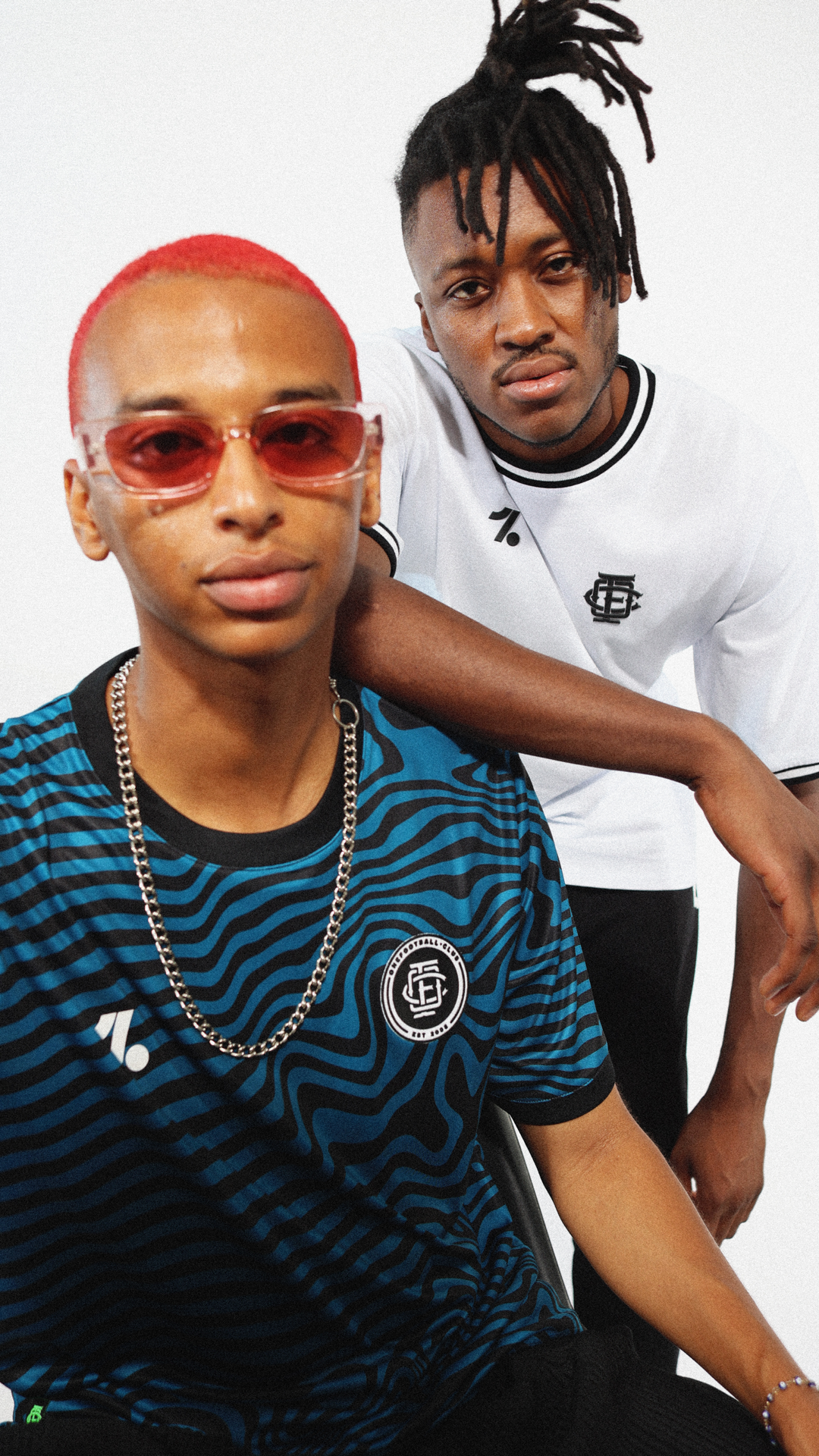 Two young Black men in fashionable sportswear posing in front of a white backdrop, showcasing a modern and urban aesthetic.