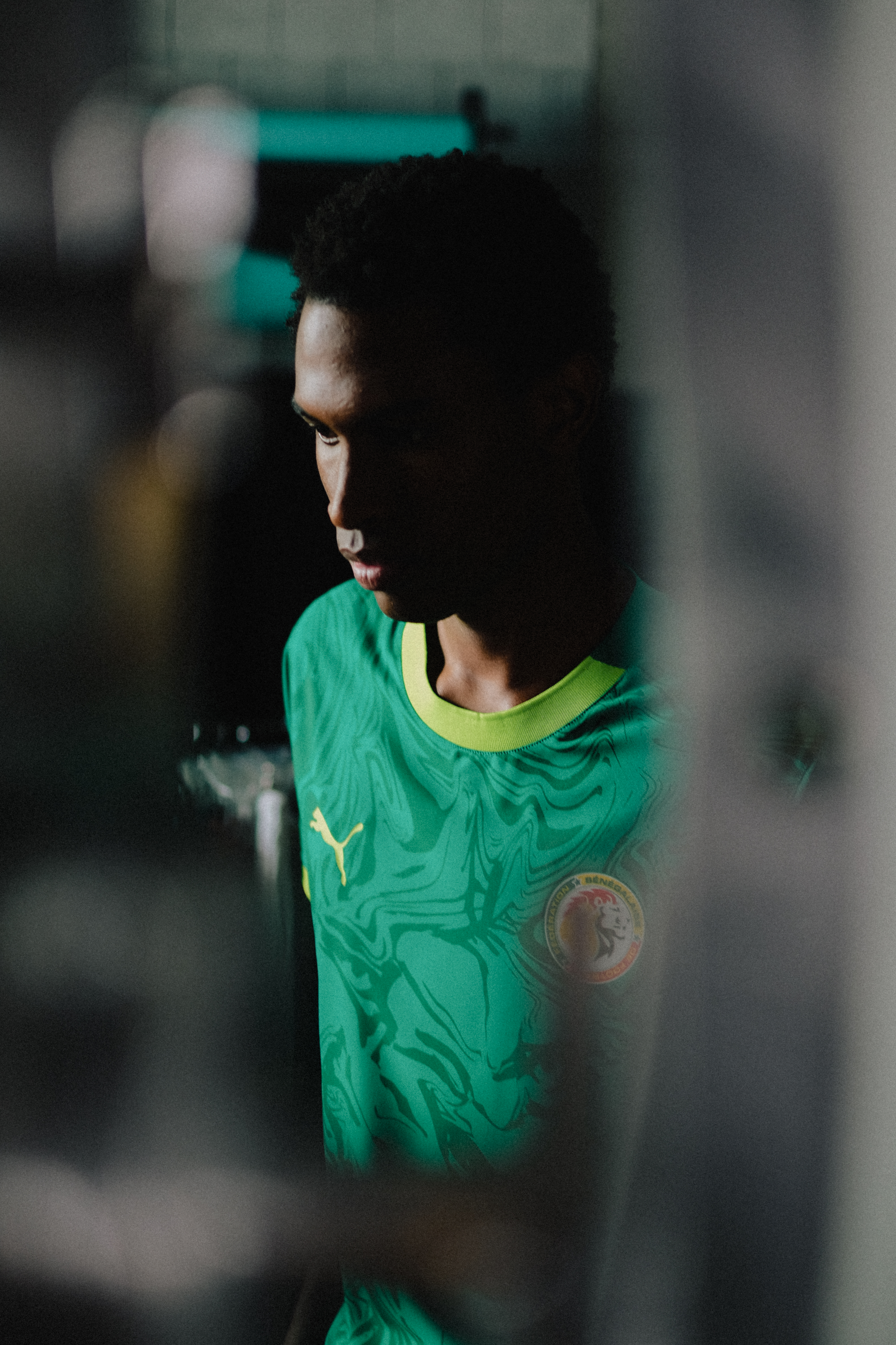 Portrait of a young adult male soccer player in a green jersey with a yellow collar, posing indoors.