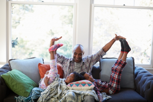 Father and two children, boy and girl, playfully pose on a sofa in pajamas, creating a sense of joyful family time inside a cozy home.