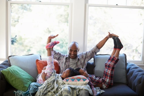 Father and two children, boy and girl, playfully pose on a sofa in pajamas, creating a sense of joyful family time inside a cozy home.