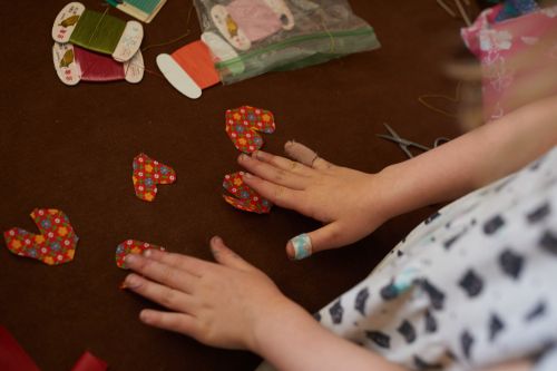 Child's hands working with heart-shaped fabric pieces on a brown surface with sewing supplies, creating a crafting project.