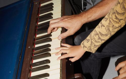Adult and child playing a piano, showing their hands on the keys, close-up view with the vintage-style piano filling the frame.