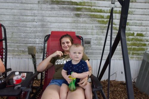 Woman seated outdoors in a red lounge chair holding a toddler holding a green sippy cup
