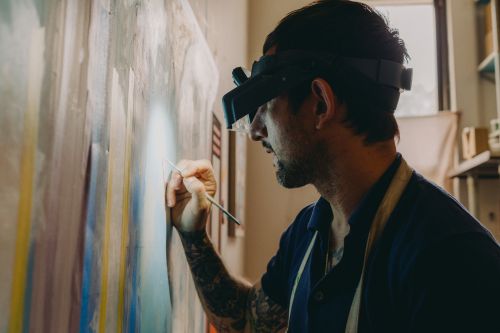 Artist painting on a large canvas in an art studio, wearing a magnifying headset for detail work, showcasing creativity and craftsmanship.