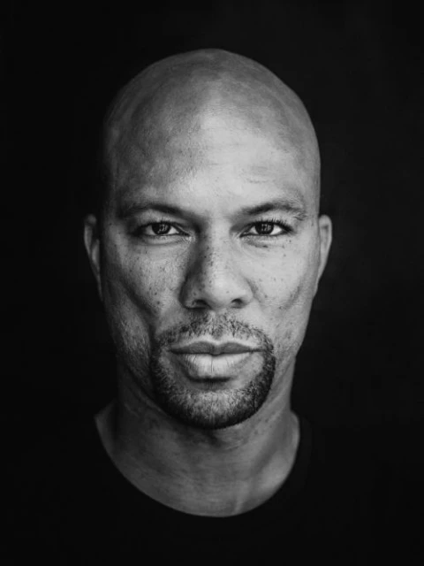Striking black and white portrait of a bald African-American man with a goatee, set against a dark background with soft, diffused lighting.