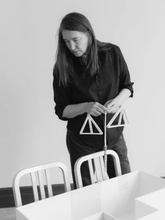 Woman in dark shirt standing at a white model table holding triangular objects, by Dustin Aksland
