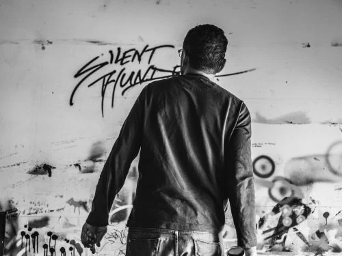 Man with back to camera in front of graffiti wall with long-sleeve shirt, jeans. Urban artistic scene with street art vibe in black and white.