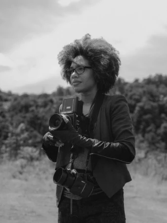 Black and white portrait of a woman with curly hair wearing glasses holding a medium format camera