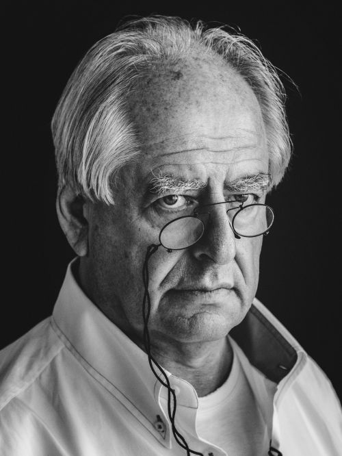 Black and white portrait of an older man with white hair wearing pince-nez glasses and a white collared shirt against a dark background.