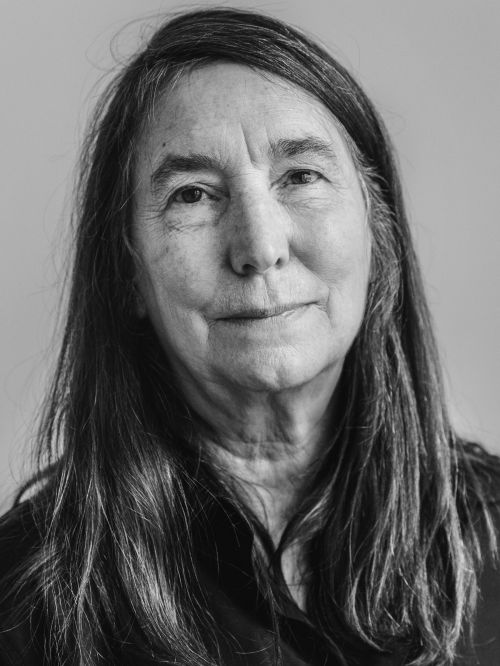 Portrait of an elderly woman with long dark hair and a neutral expression against a plain background