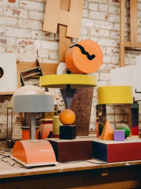Geometric shapes and furniture including a table lamp arranged on a wooden surface in front of a brick wall in a studio environment.