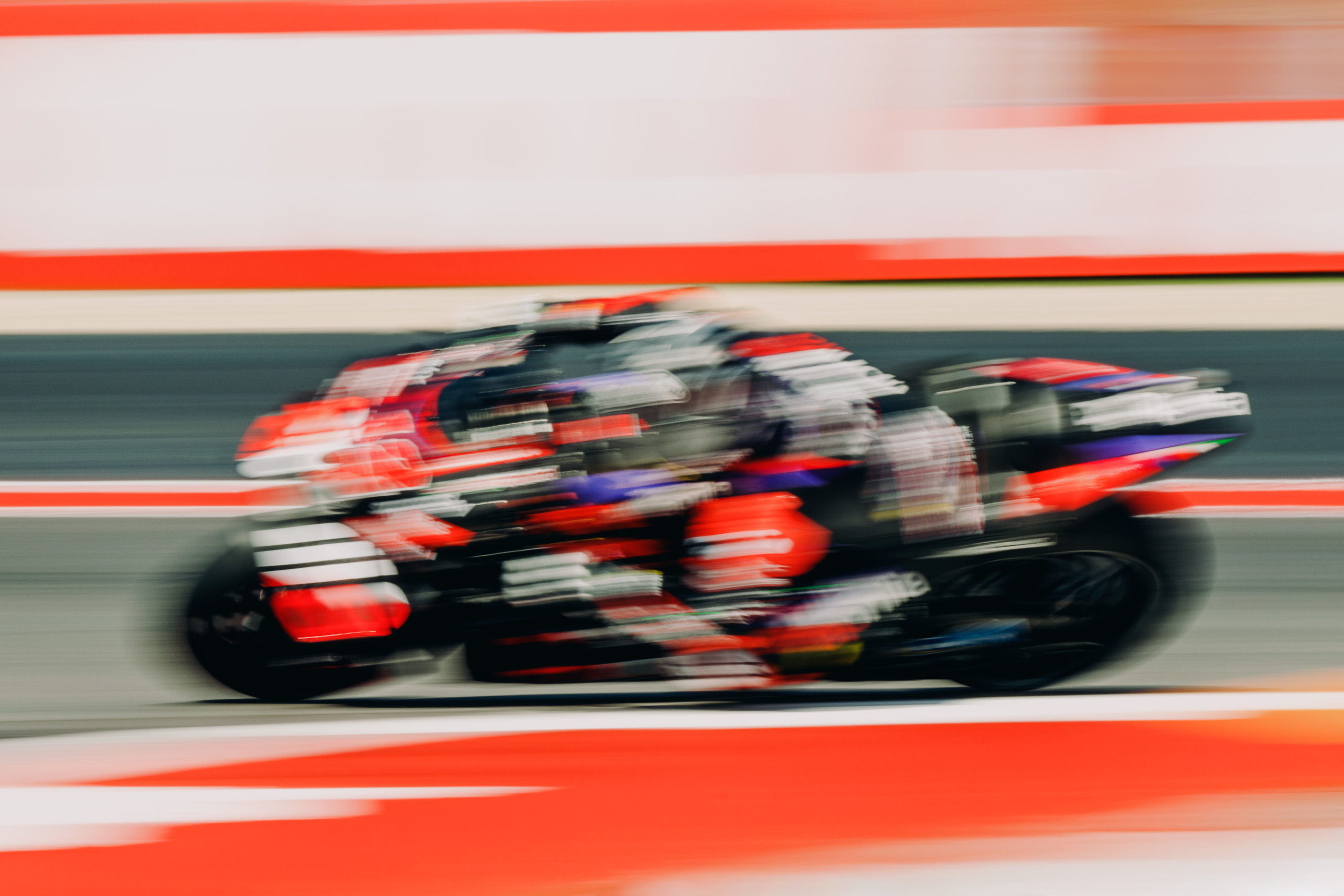 Motion blur shot of a motorcycle racer speeding on a track with red and white borders, capturing the essence of speed and competition.