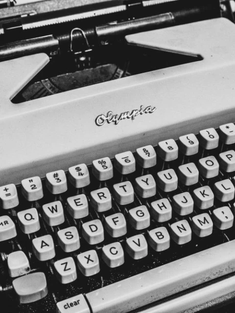 Close-up of a vintage Olympia typewriter with visible keys and brand name, in a black and white composition, showcasing a retro aesthetic.