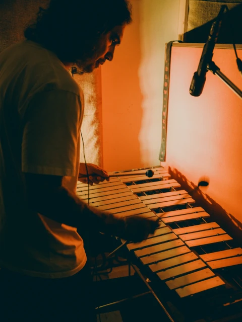 Man plays the xylophone in a warm-lit studio. The musician uses mallets to strike the metal bars of the instrument indoors.
