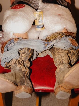 Close-up shot of cowboy boots, lowered denim jeans, ice bags on legs, and a beer can by Dustin Aksland