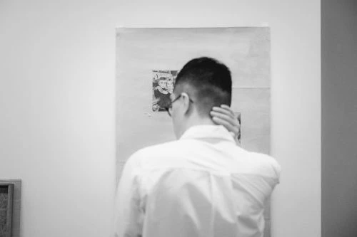 Monochrome rear view of a man in a white shirt touching his neck while viewing art gallery exhibits.