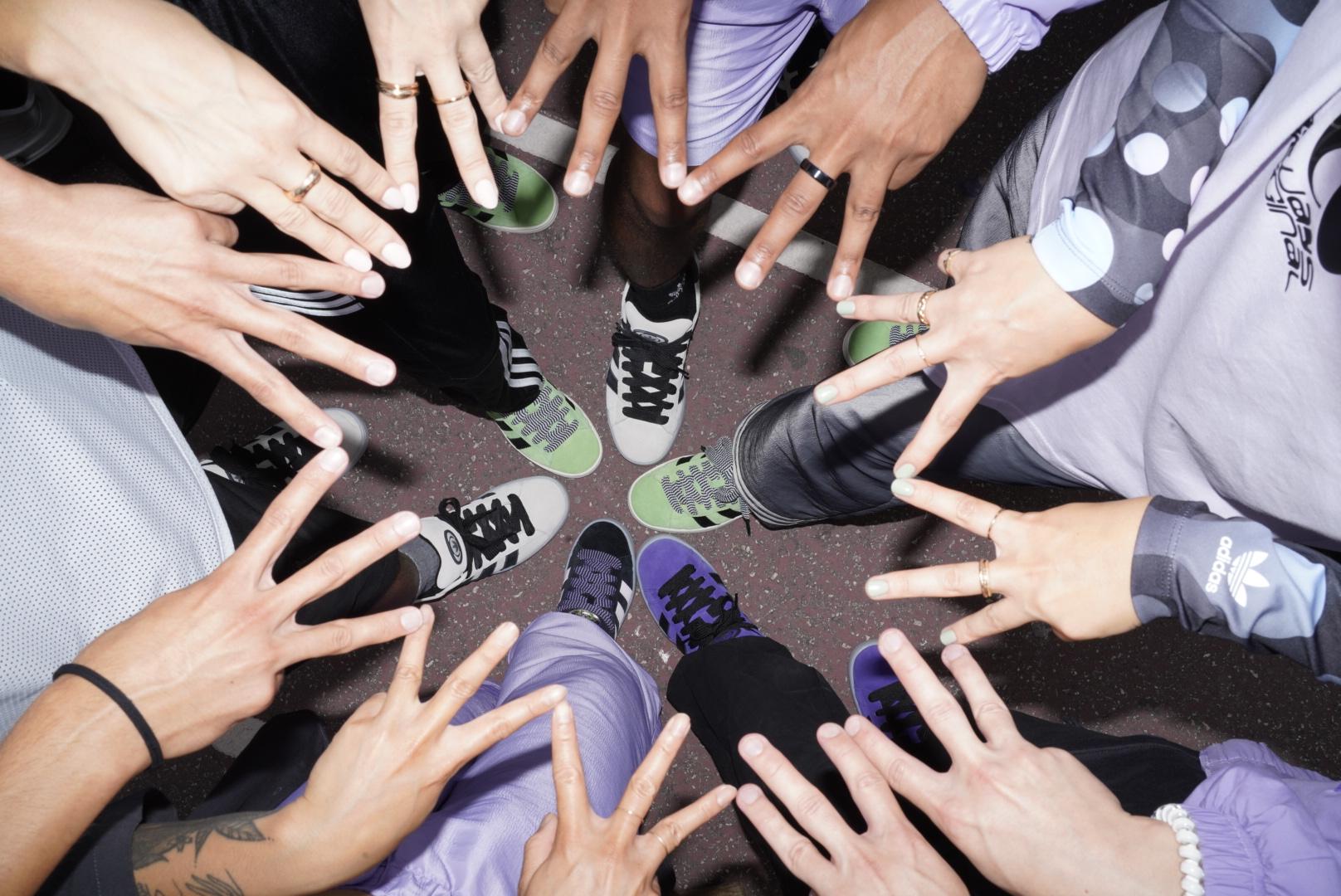Overhead shot of diverse group forming star with hands and feet around Adidas sneakers in a circle; lifestyle, fashion, and sport.