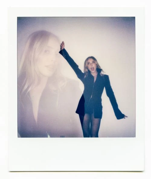 Polaroid-style portrait of a woman in a dark jacket, captured in a double exposure against a white backdrop, creating a layered, vintage effect.