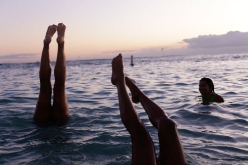 Three people are in the ocean, with two people's legs sticking straight up out of the water, and a third person swimming nearby.