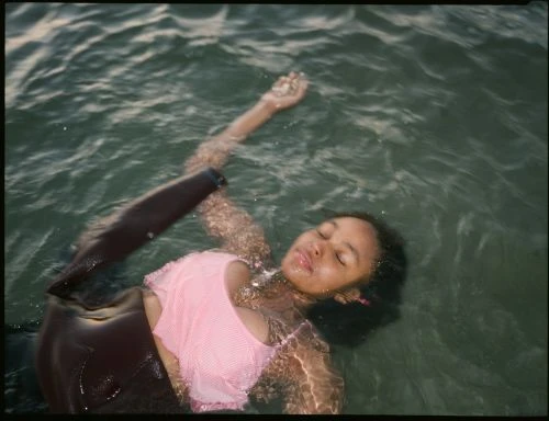 Young woman in a pink top floats in shimmering ocean water with her eyes closed, creating a serene and reflective portrait.