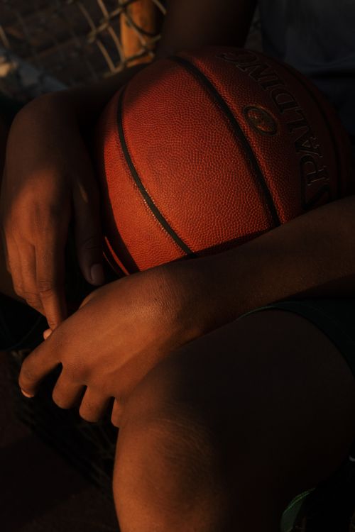 Close-up of an African American person's hands holding a basketball with the Spalding logo visible, featuring warm, golden lighting.
