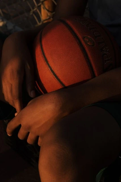 Close-up of an African American person's hands holding a basketball with the Spalding logo visible, featuring warm, golden lighting.