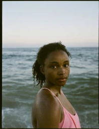 A Black woman in a pink swimsuit looking back at the camera standing waist-deep in the ocean.