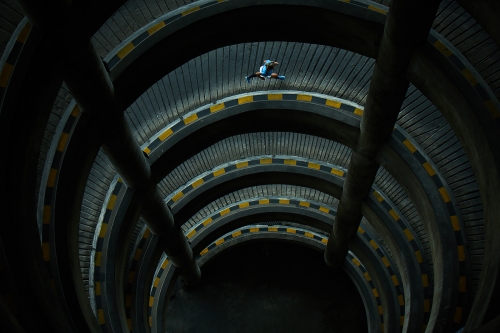 A person skateboarding in a parking garage with yellow and black stripes on the wall creating a dizzying, tunnel-like perspective.