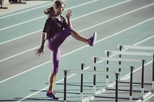 Athletic woman in sportswear does hurdle drills on a running track with track lines and rows of hurdles in outdoor setting.