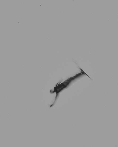 Black and white shot of an adult, with a water ski, performing a trick in the air, over water.