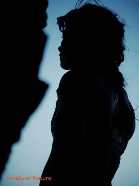 Silhouette of a woman, side profile with wavy hair, standing outdoors against a light blue background; 'Freaks of Nature' text visible.