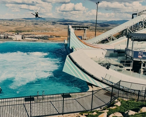 A freestyle skier performs a jump during training on a ski jump with a swimming pool in the summer, showcasing the sport of freestyle skiing.