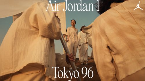 Group of people in light-colored clothing posing in an outdoor setting, promoting Air Jordan 1 shoes, with a desert-like backdrop.