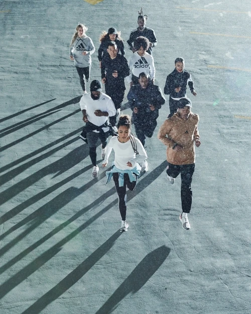 Group of diverse runners in athletic wear sprinting outdoors on gray pavement in overcast conditions, creating long shadows.