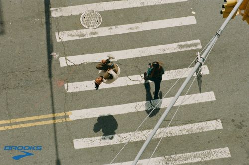 Aerial view of two women walking across a white-striped crosswalk on a city street with traffic lights, on a sunny day.