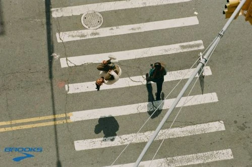 Aerial view of two women walking across a white-striped crosswalk on a city street with traffic lights, on a sunny day.