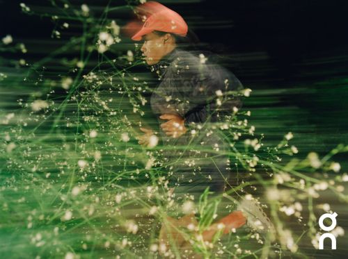 Runner in bright orange cap running past green foliage captured with long exposure motion blur